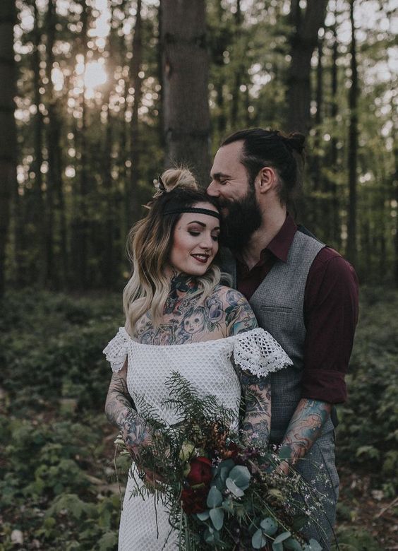 a boho couple with the groom wearing a burgundy shirt and a grey waistcoat and pants, cuffed sleeves to show off the tattoos