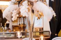 a bold art deco party table with a tall centerpiece of feathers, orchids and candles around, white and silver place settings