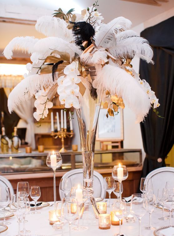 a bold art deco party table with a tall centerpiece of feathers, orchids and candles around, white and silver place settings