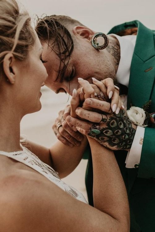 a bold groom's look with an emerald suit, a white shirt and bold hand and neck tattoos is wow