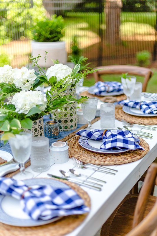 a bright and cool bbq rehearsal dinner tablescape with white hydrangeas and greenery, candleholders, woven placemats and plaid napkins