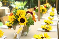 a bright bbq rehearsal dinner table with a colorful sunflower and citrus centerpiece and sunflowers marking each napkin