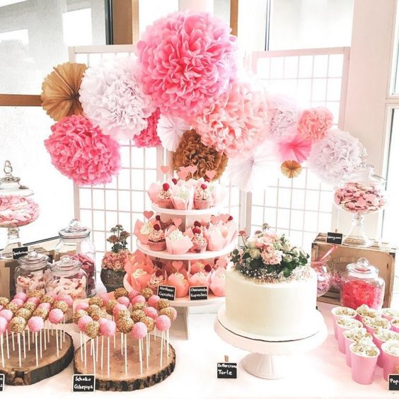 a bright pink candy table with wood slice pop stands, a lush paper pompom garland and jars with candies and sweets