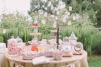 a candy table with pastel candies in jars, bowls and stands and a whimsy tree candle stand
