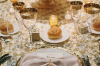 a chic 1920s tablescape with a white flower and feather centerpiece, gold rim glasses, candles and buns, gold rim chargers and pearls that tie the napkins