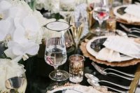 a chic and glam art deco tablescape with a black table, copper placemats, black and white plates, white blooms and chic glasses