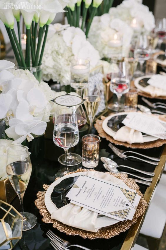 a chic and glam art deco tablescape with a black table, copper placemats, black and white plates, white blooms and chic glasses