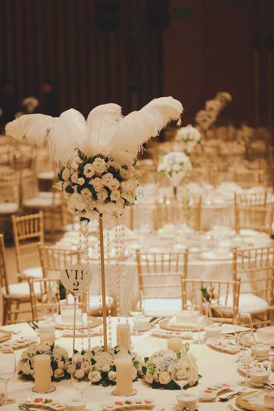 a chic neutral table setting in 1920s style, with a tall white rose centerpiece with feathers, candles and pearls and white place settings