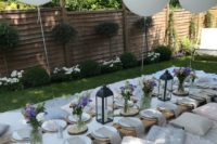 a chic white garden picnic setting with white blankets, neutral pillows, white balloons, bright blooms and a low pallet table