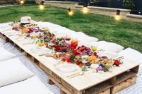 a colorful boho picnic with a low table, neutral textiles, bright blooms and candles, string lights over the table