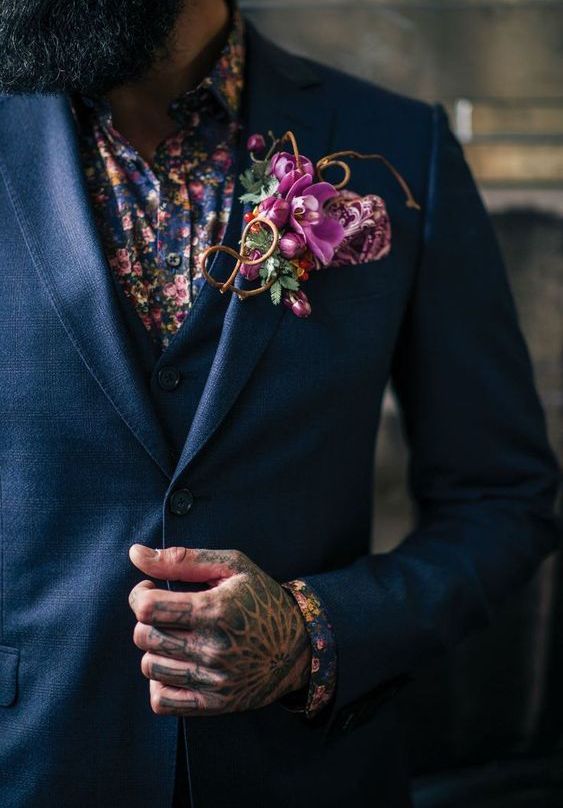 a colorful groom's look with a blue three piece pantsuit, a colorful floral shirt and a bold orchid boutonniere, a bold hand tattoo