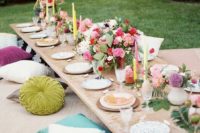 a colorful rehearsal picnic setting with bright blooms and candles, colorful pillows and porcelain