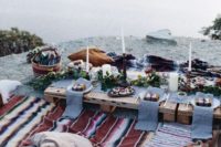 a cool lake picnic setting with a low table, colorful boho rugs, neutral candles and greenery and bright blooms