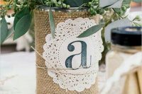a cool rustic centerpiece of a tin can with burlap and a doily, greenery, leaves and white blooms for a bbq rehearsal dinner