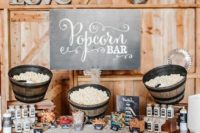 a cozy rustic popcorn bar with wooden baskets with popcorn, candies, sprinkles and toppings and chalkboard signage