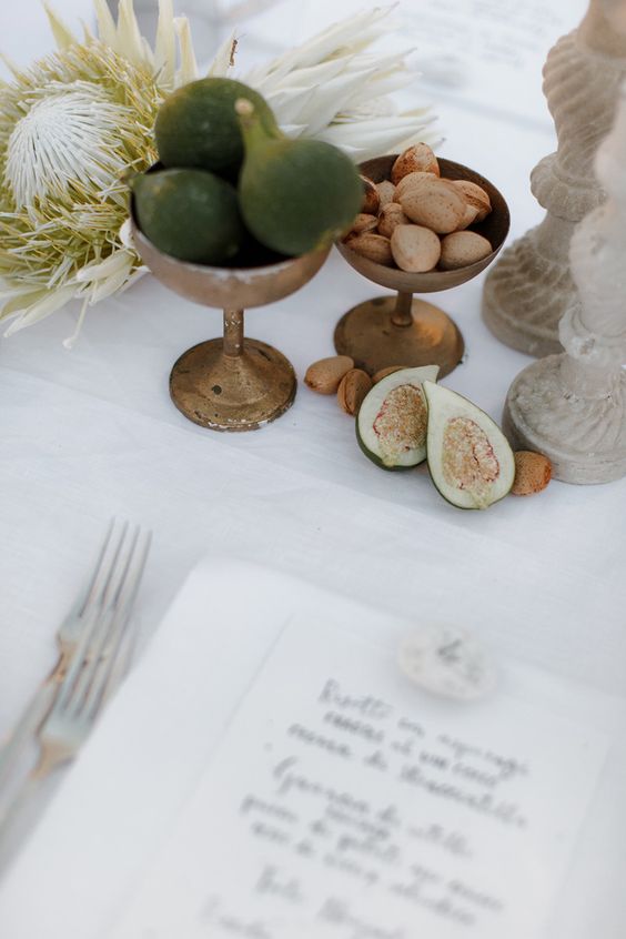 a creative cluster wedding centerpiece of vintage bowls with figs, nuts, a tropical protea and some candles