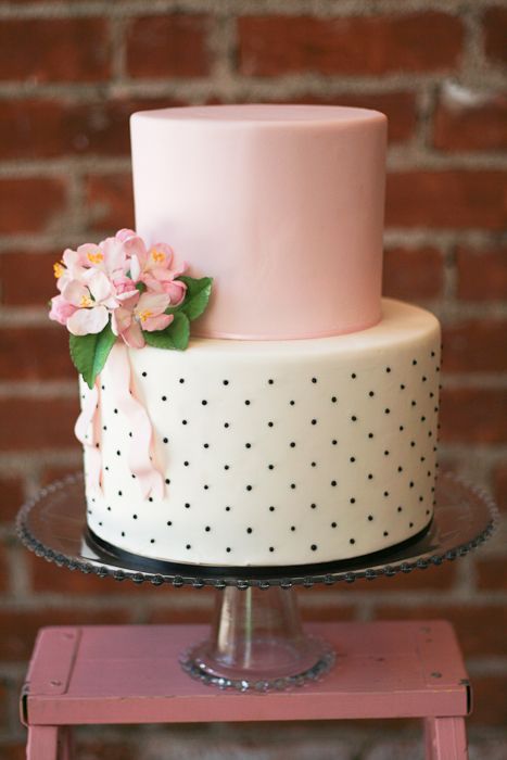 a cute wedding cake with a plain pink and black and white polka dot tier, pink blooms and greenery and ribbons is amazing for spring or summer