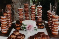 a donut station with donut son holders and metallic trays, a cake topped with fresh blooms and lots of delicious donuts