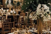 a glam and chic art deco tablescape with a black sequin tablecloth, gold placemats, a white bloom and greenery centerpiece and gold rim glasses