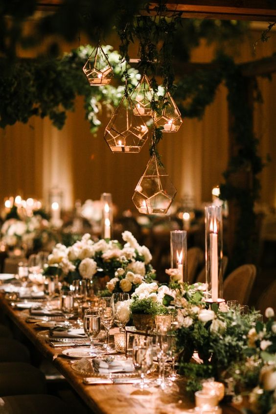 a glam and refined art deco tablescape with white blooms and greenery, candles in faceted candleholders and gold chargers and cutlery