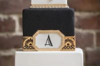 a gorgeous black and white square cake with gold geo decor, vintage brooches and beading and feathers