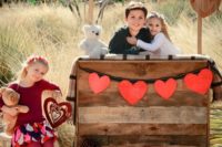 a kissing booth of pallets, with a heart bunting, a chalkboard sign, plush toys and blankets is a cute idea