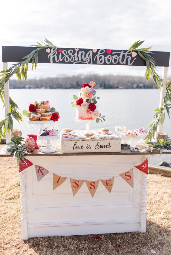 a kissing booth that doubles as a dessert table, with greenery, a burlap bunting and delicious sweets