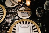 a lovely black, white and gold tablescape with a sequin tablecloth, gold chargers and striped plates, a white centerpiece and candles around