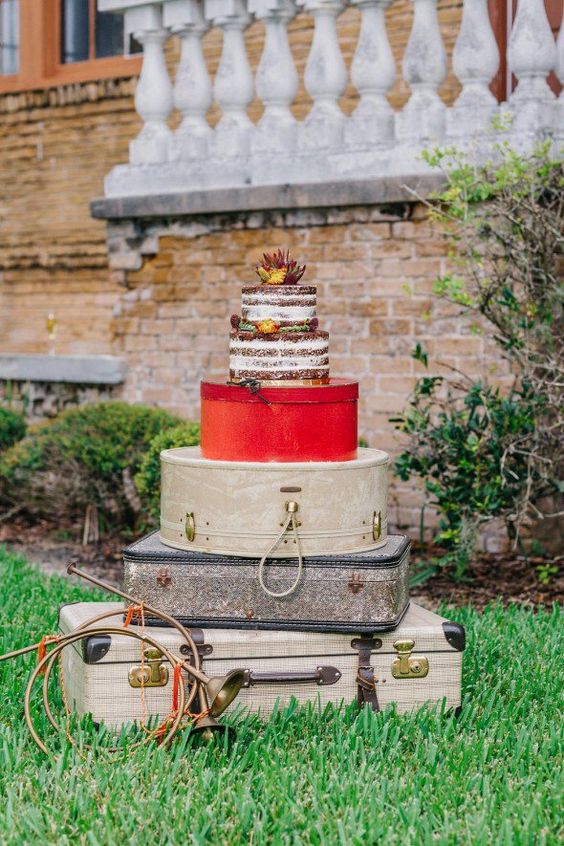 a lovely stack of vintage suitcases substituting a wedding cake table, with a naked wedding cake on top is amazing
