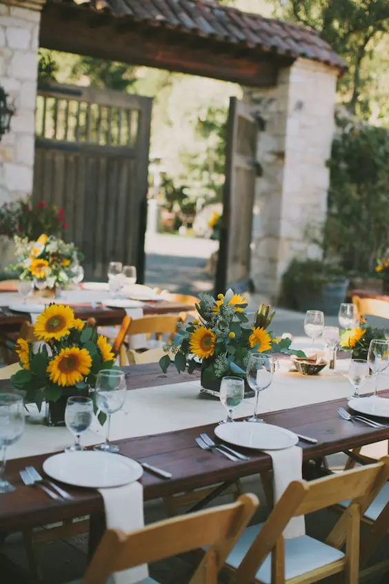 a lovely wedding tablescape with bright sunflower centerpieces and white linens is elegant and simple at the same time
