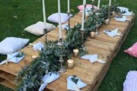 a low pallet table with a lush greenery runner, candles and white napkins plus neutral and pink pillows