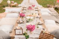 a neutral boho picnic setting with a low pallet table, neutral textiles, pink blooms, a LOVE sign and string lights over the table