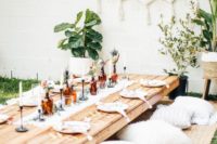 a neutral boho picnic with a low table, fur pillows, leather ottomans, potted greenery, greenery and feathers in bottles and macrame