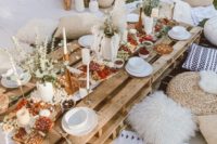 a neutral boho picnic  with a pallet table, printed blooms, rugs, greenery, pampas grasss and neutral textiles