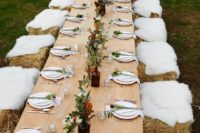 a neutral rustic tablescape with hay and fur stools, greenery and dark blooms, string lights over the table