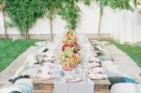 a neutrla garden picnic setting with a low wooden table, neutral textiles and bright blooms and greenery plus copper chargers