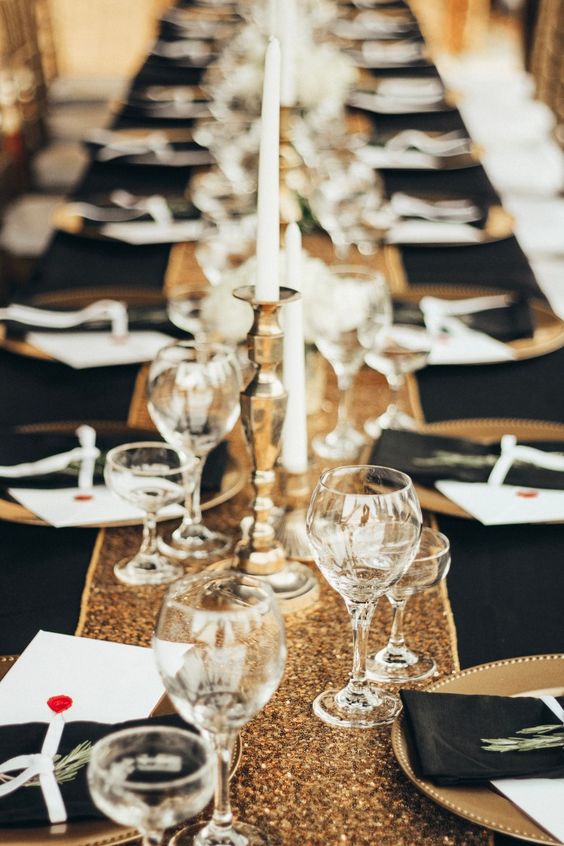 a pretty and glam 1920s tablescape with a black tablecloth and a gold sparkling runner, gold chargers and black napkins