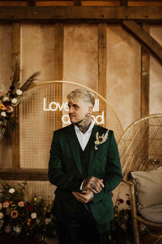 a refined groom's look with a white shirt, a dark green three piece suit and hand and neck tattoos that strike