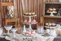 a rustic meets vintage candy table with a doily tablecloth, a rustic table, a burlap banner, sweets and cupcakes on a chair and crates