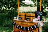 a rustic popcorn bar of stained wood, with wooden baskets for popcorn, toppings and baskets with crackers and candies
