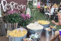 a rustic popcorn bar with buckets and bathtubs with popcorn and toppings and some potted blooms