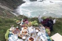 a simple rustic picnic setting with a lwo wooden table, plaid textiles, some hydrangeas, candles and lots of food