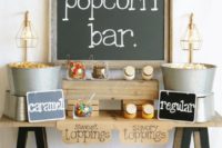 a simple rustic popcorn bar with chalkboard signage, popcorn in buckets, colorful sprinkles in jars
