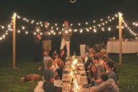 a simple rustic rehearsal dinner picnic with a low table, candle lanterns, lights and blooms is a cozy event
