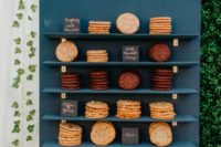 a stylish navy cookie wall with shelves nd various types of cookies, each marked with a little sign