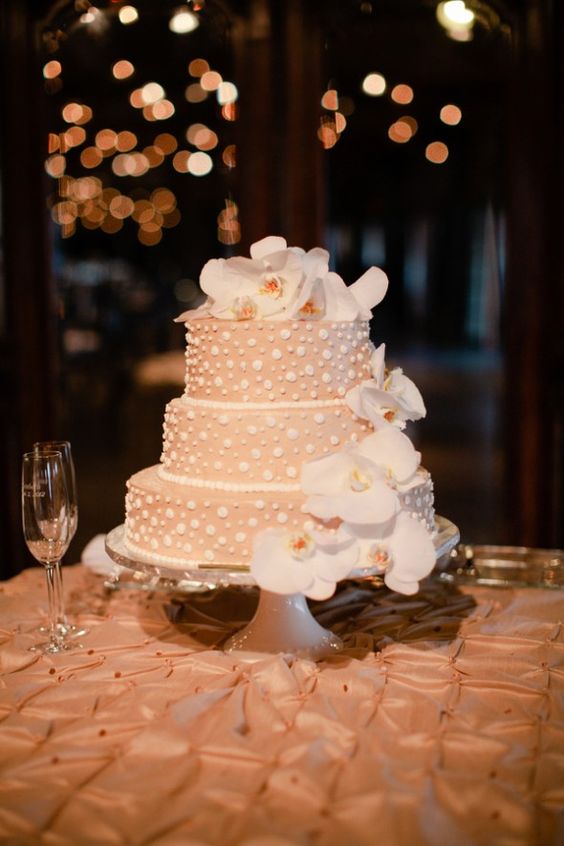 a tan wedding cake with white mismatching polka dots and white orchids is a stylish and elegant idea for a modern neutral wedding