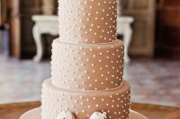 a tan wedding cake with white polka dots, white blooms on top and pretty sugar penguin toppers placed on the bottom is amazing