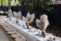 a trendy neutral boho picnic with pampas grass, candles, pastel and neutral textiles and jute ottomans