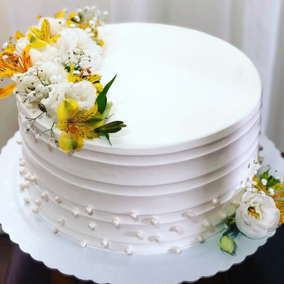 a white buttercream wedding cake with pearls as polka dots, white and yellow blooms and greenery is a chic and lovely idea