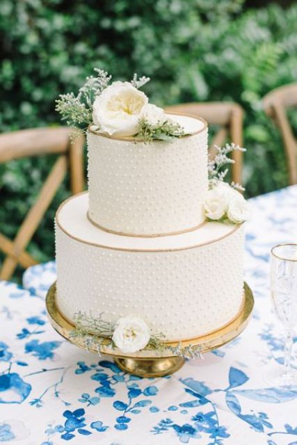 a white polka dot wedding cake with gold trims, white blooms and greenery is a stylish and chic idea for a neutral spring or summer wedding